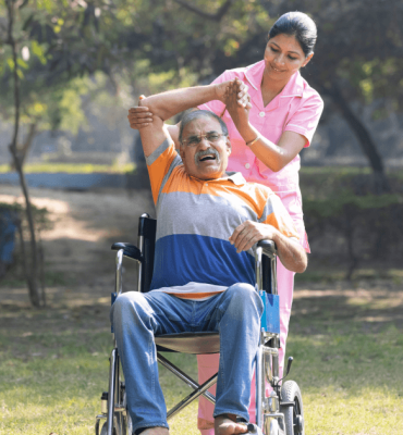 Caregiver helping elderly man in wheelchair with physiotherapy exercise outdoors