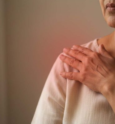 A close-up of an elderly woman holding her shoulder in discomfort, illustrating bone or joint pain associated with osteoporosis.