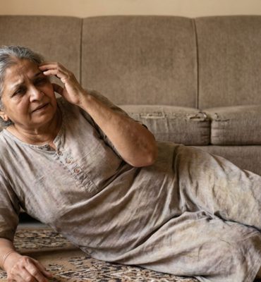 An elderly woman showing signs of a medical emergency; she has fallen to the rug and appears disoriented, illustrating the sudden onset of stroke symptoms.