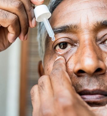 An older man carefully administering medicated eye drops into his lower eyelid to manage eye pressure.