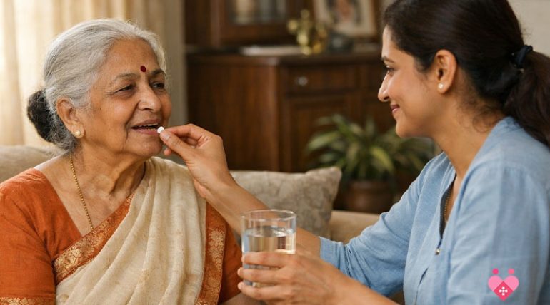 A young female caregiver assisting an elderly Indian woman with her medication by offering a pill and a glass of water in a comfortable home setting.